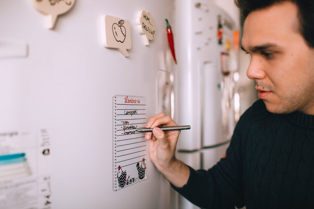 young man writing reminder on fridge note
