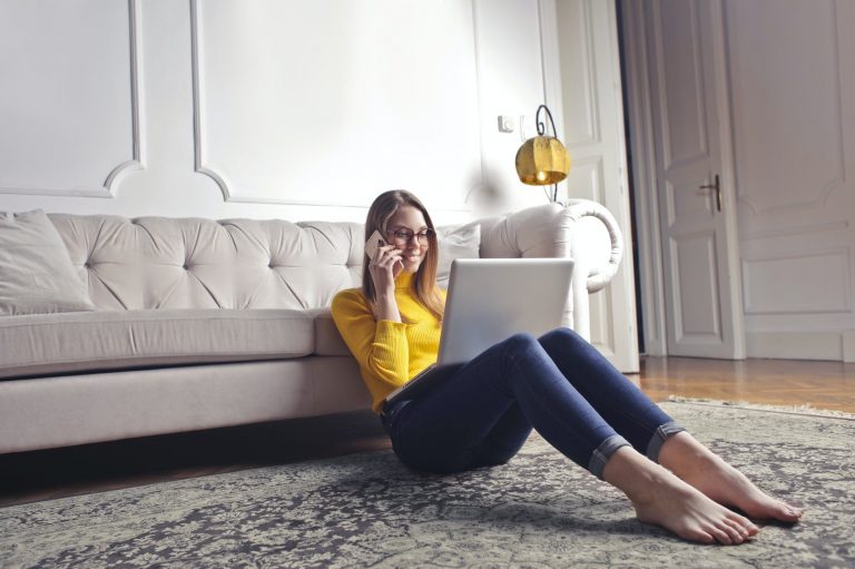 happy adult woman talking on phone and using laptop while chilling at home