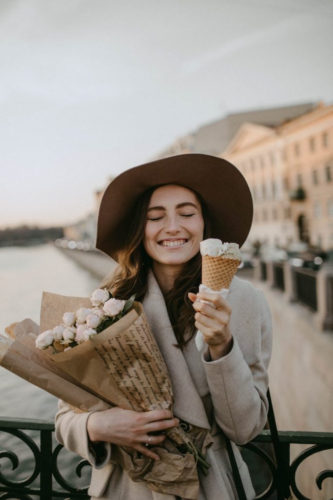 woman wearing brown coat holding white flower bouquet and ice cream