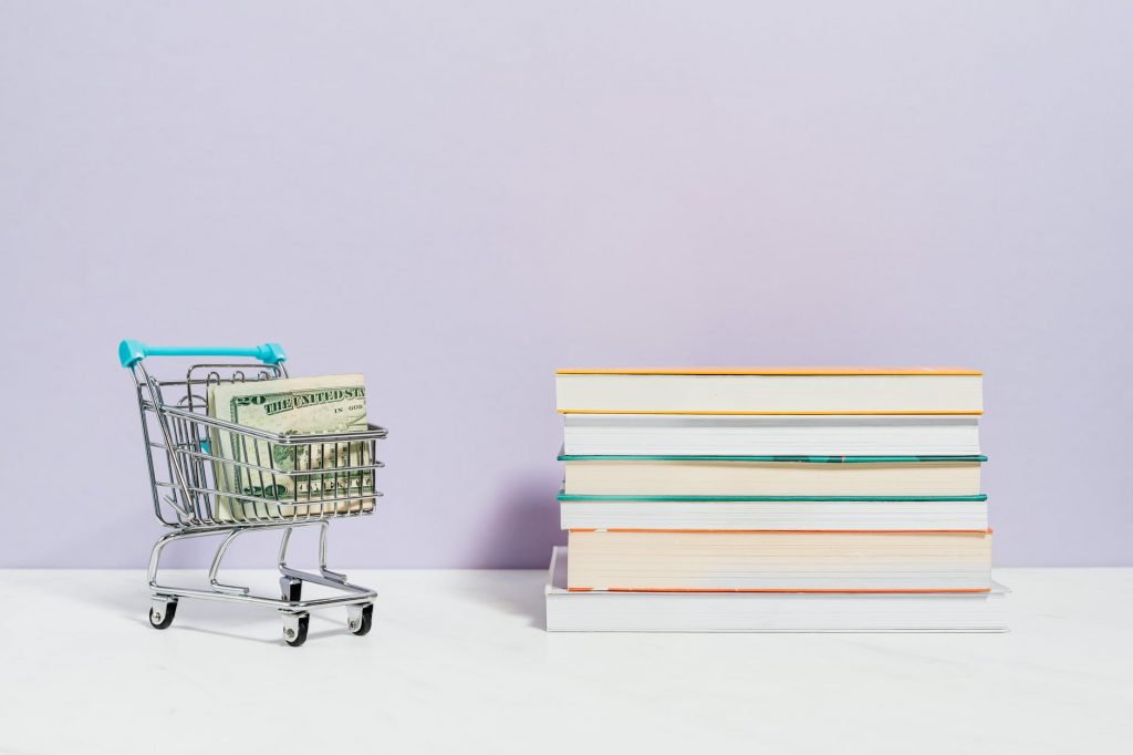 stack of books beside a shopping cart with cash money