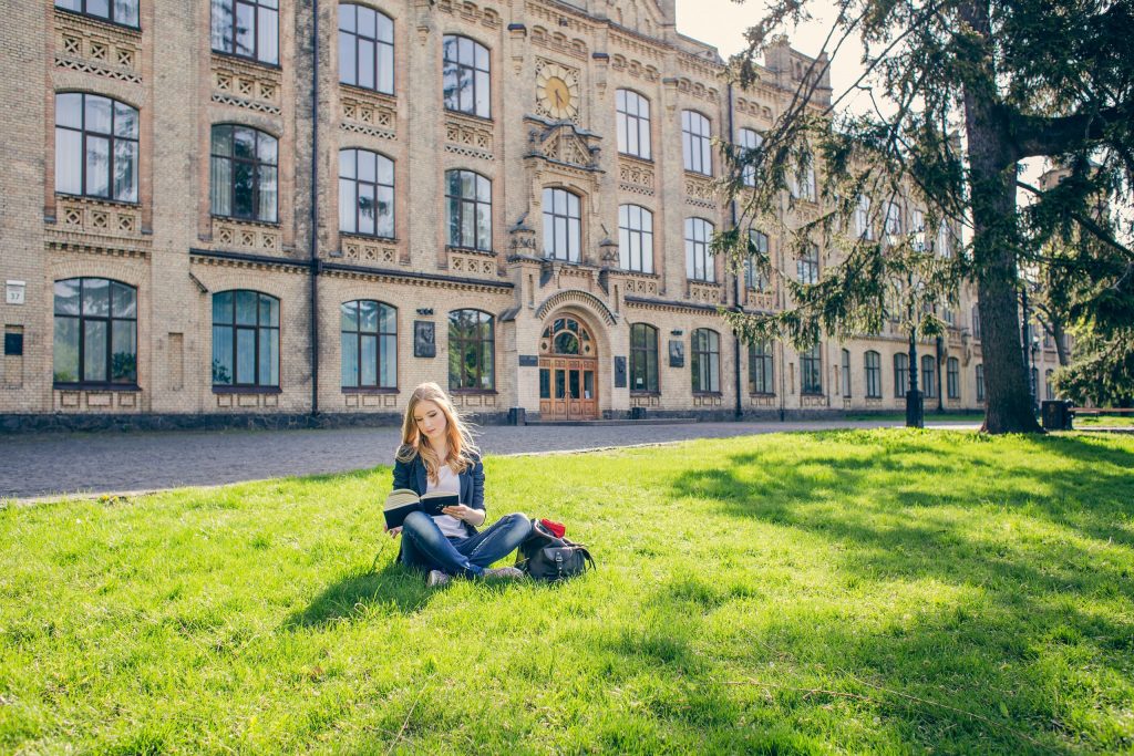 student reading on the grass of a college campus