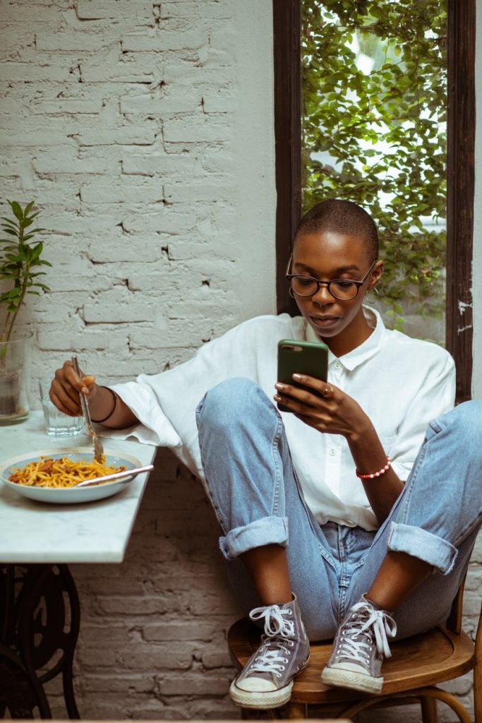 focused black woman having lunch and browsing smartphone
