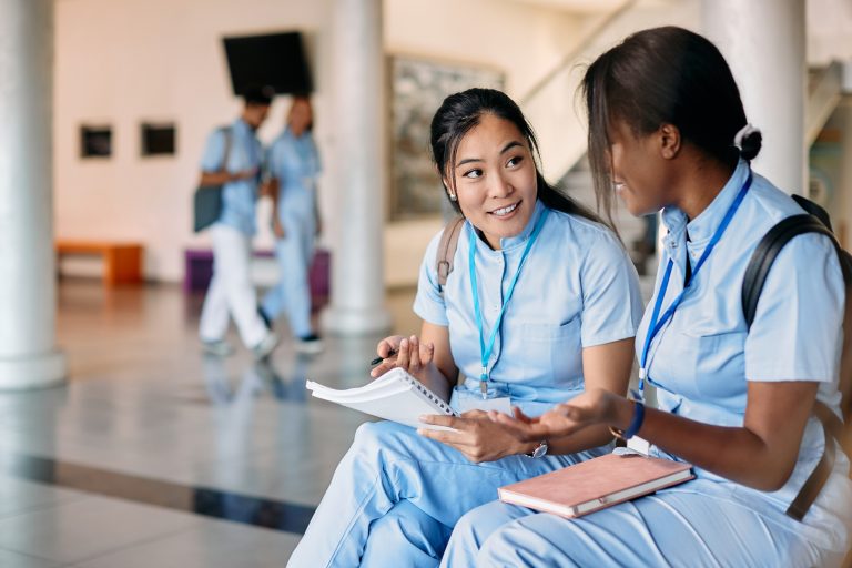 Asian nursing student and her female friend talk while studying in hallway at medical university.