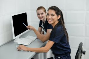 Two female nurse students pointing to a computer and smiling at the camera