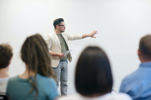 Man talking to a group of people pointing to a white board