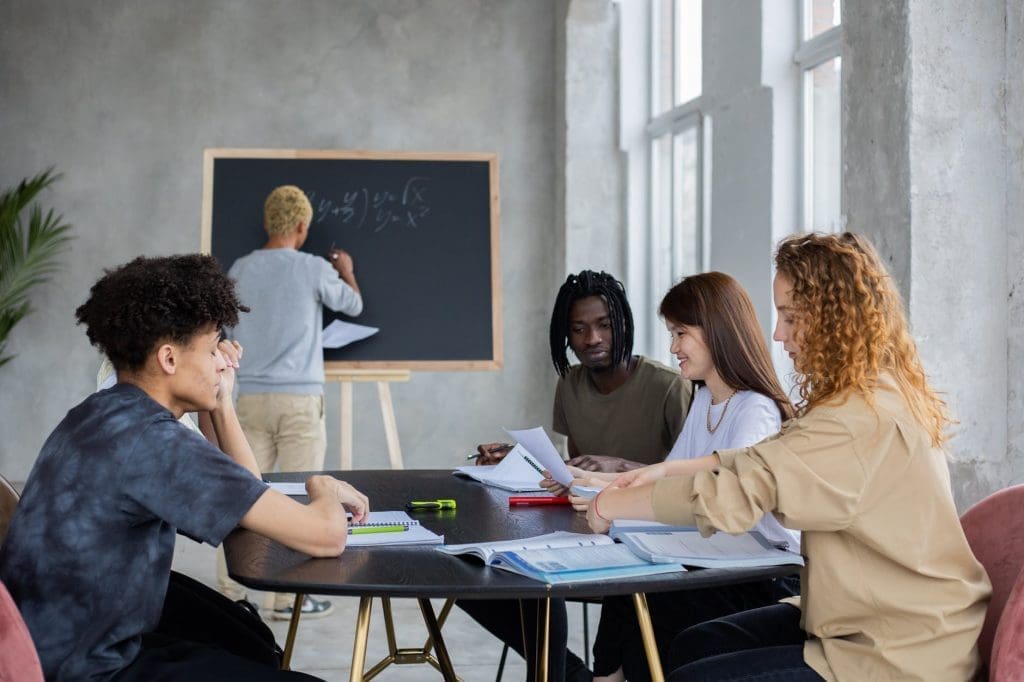 anonymous man writing on chalkboard near group of diverse students at table