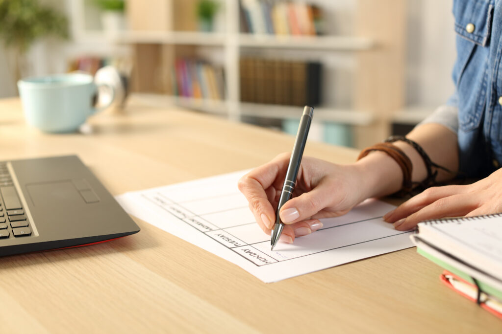Close up of student girl hand writing schedule on weekly planner on a desk at home