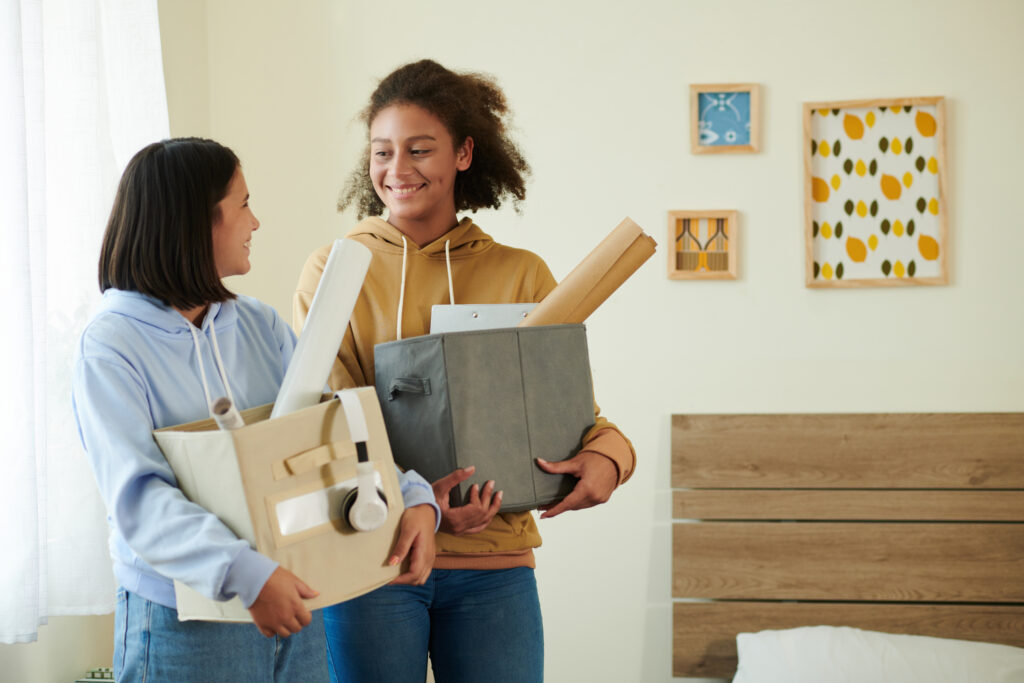 Smiling teenage roommates with boxes of belongings meeting each other for the first time